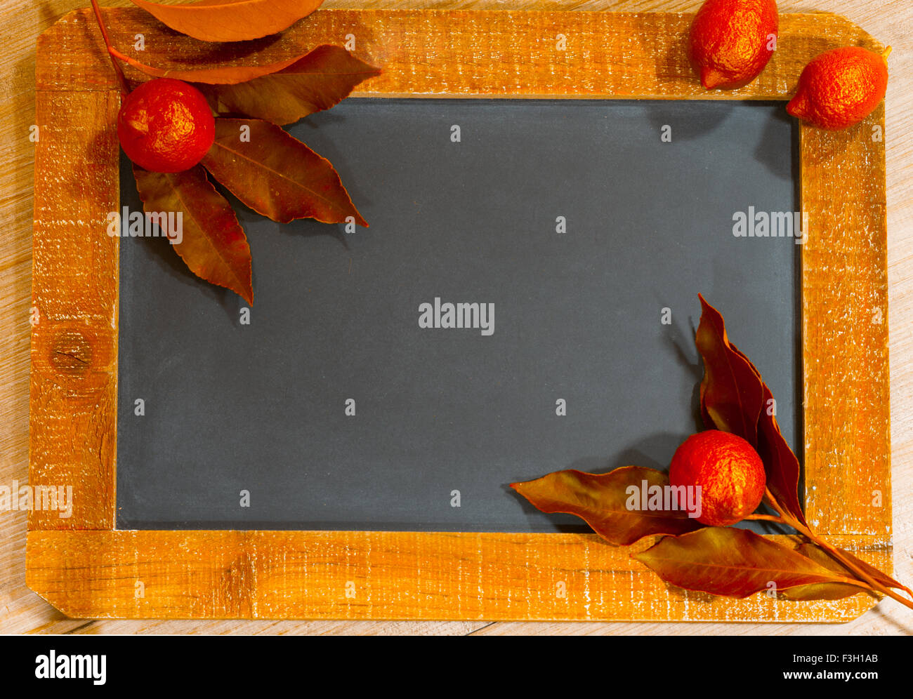 rote Zitronenblätter und Zitrusfrüchte auf einer Schiefertafel Tafel Stockfoto