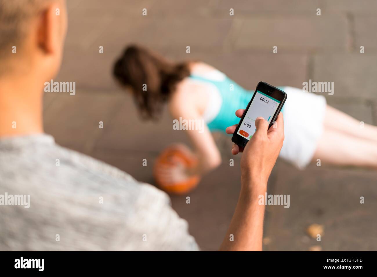 Schulter-Blick über männliche Trainer Timing Läuferinnen Push-Ups auf smartphone Stockfoto