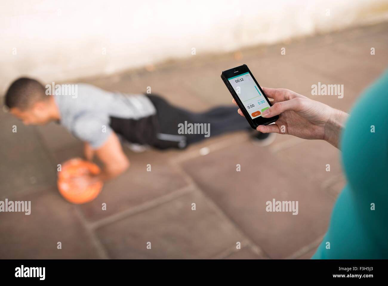 Über Schulter Blick auf weibliche Trainer Timing männliche Läufer Push-Ups auf smartphone Stockfoto