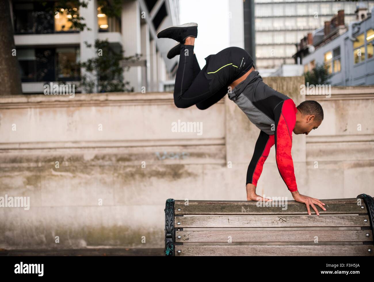 Junger Mann springen über Parkbank in Stadt Stockfoto