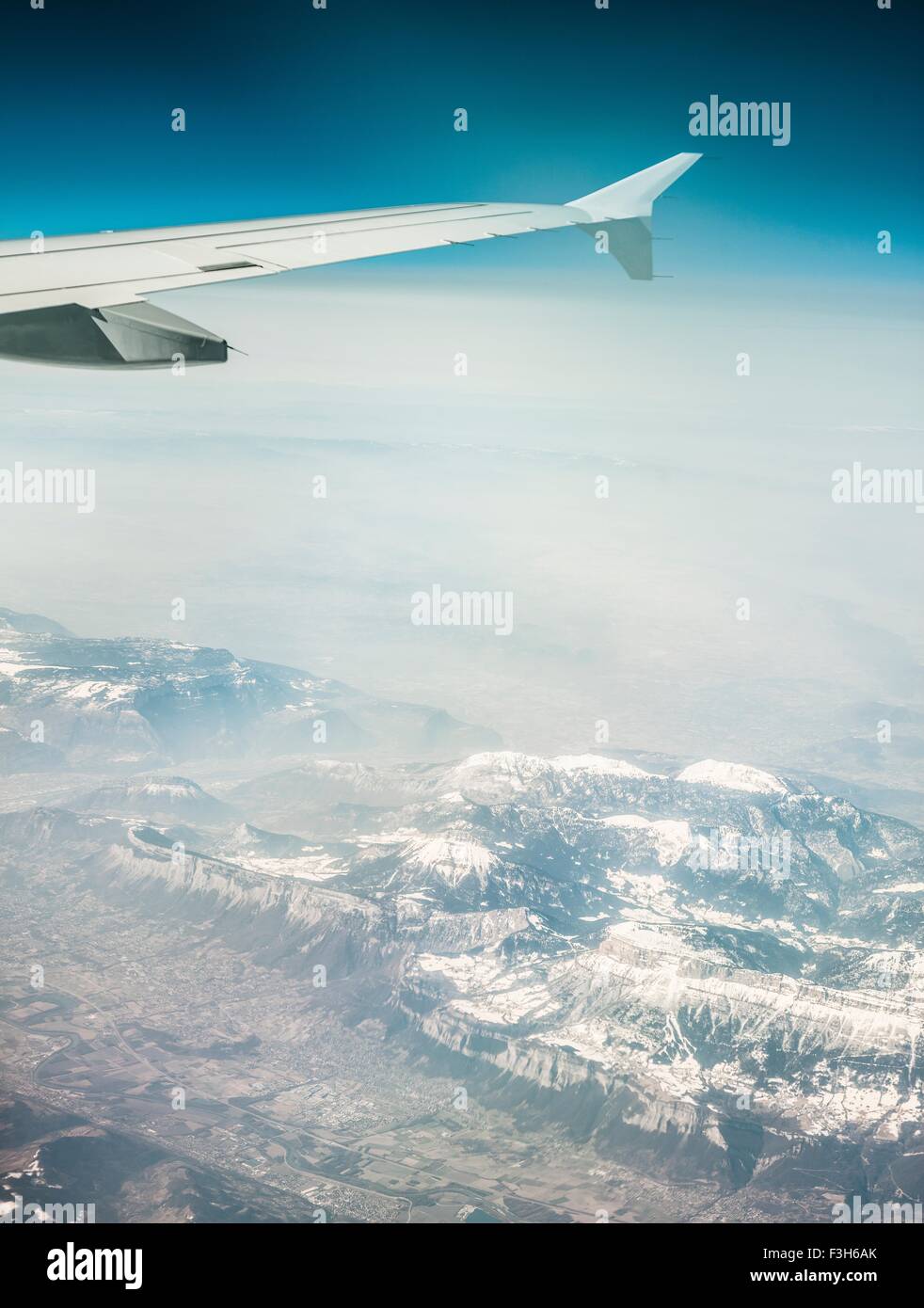 Luftbild von Flugzeugflügel und nebligen schneebedeckten Bergen Stockfoto