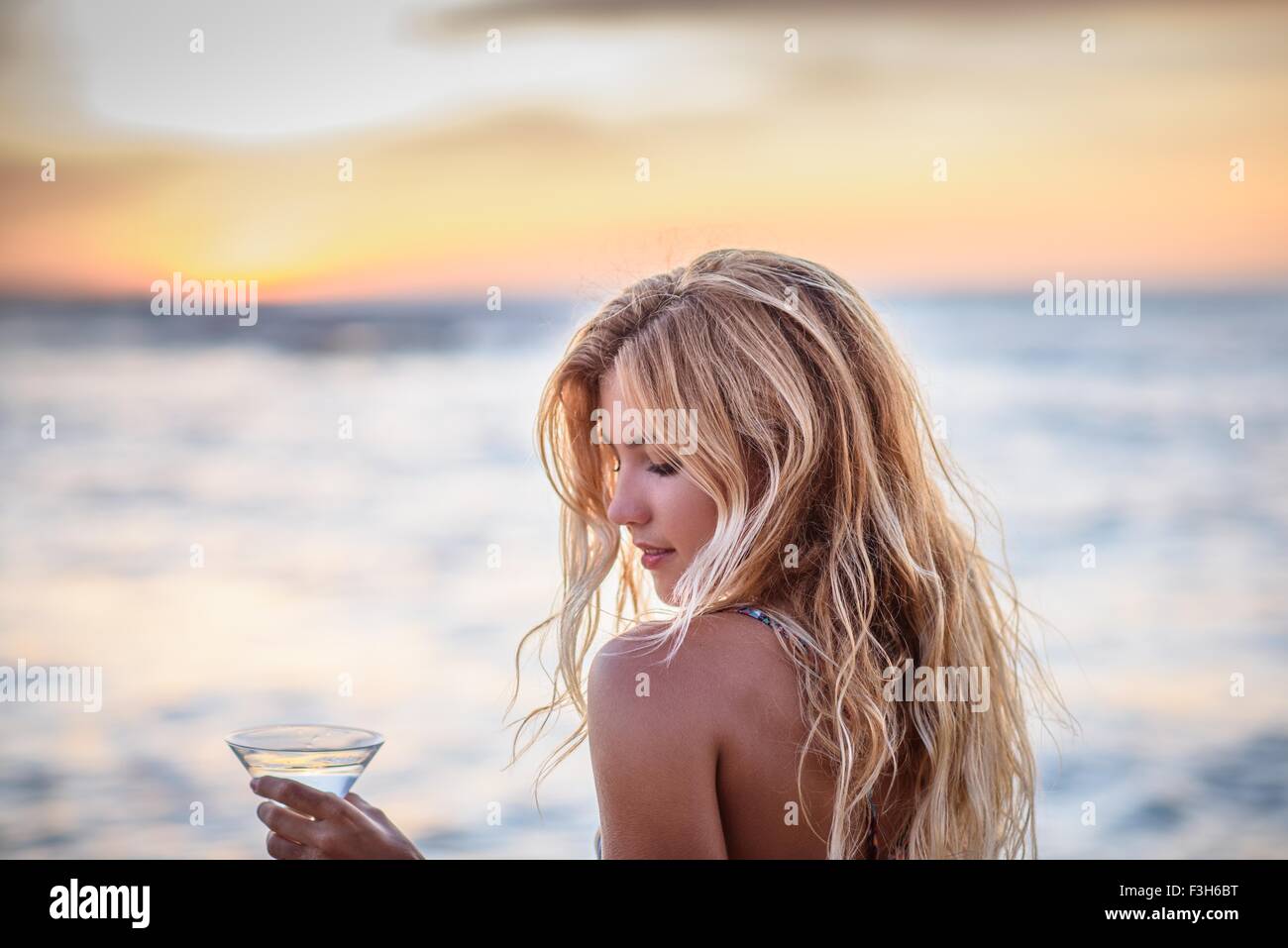 Junge Frau am Strand trinken cocktail bei Sonnenuntergang Stockfoto