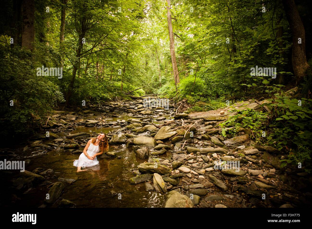 Mitte Erwachsene Frau trägt weiße Kleid sitzt auf Felsen Flussbett nachschlagen Stockfoto