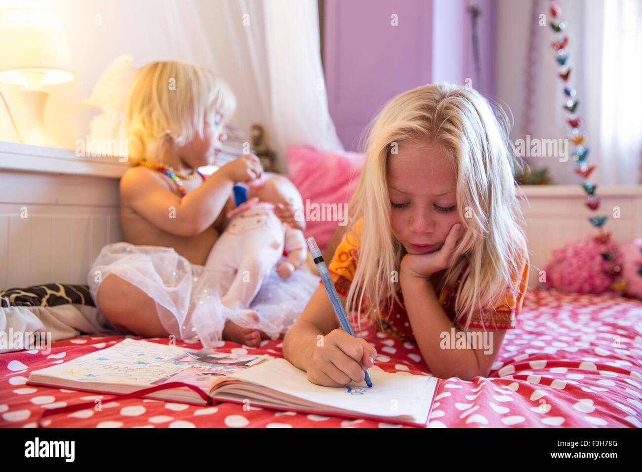 Mädchen und Kleinkind Schwester auf Bett spielen mit Malbuch Stockfoto