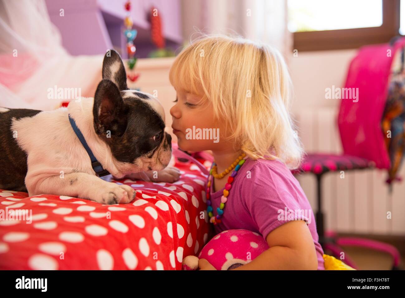 Weiblichen Kleinkind küssen niedlichen Hund im Schlafzimmer Stockfoto