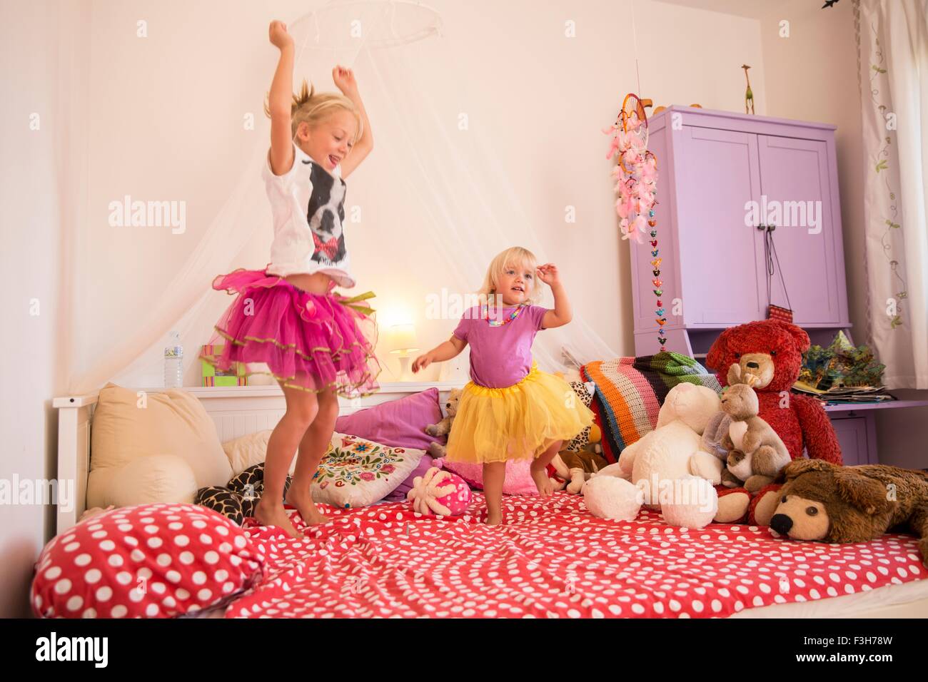 Mädchen und Kleinkind Schwester tanzen in Tutus auf Bett Stockfoto