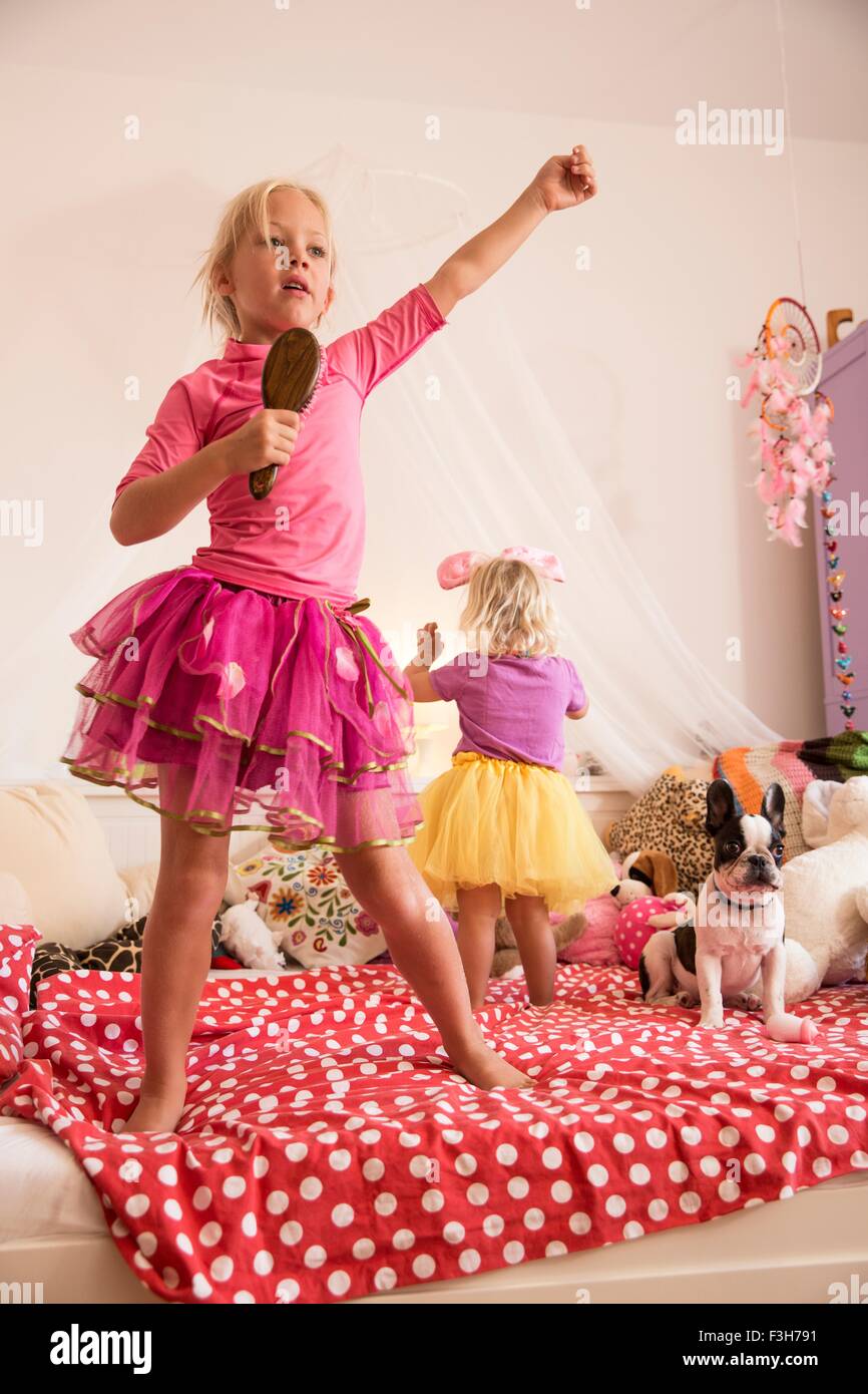 Mädchen und Kleinkind Schwester tanzend und singend auf Bett Stockfoto