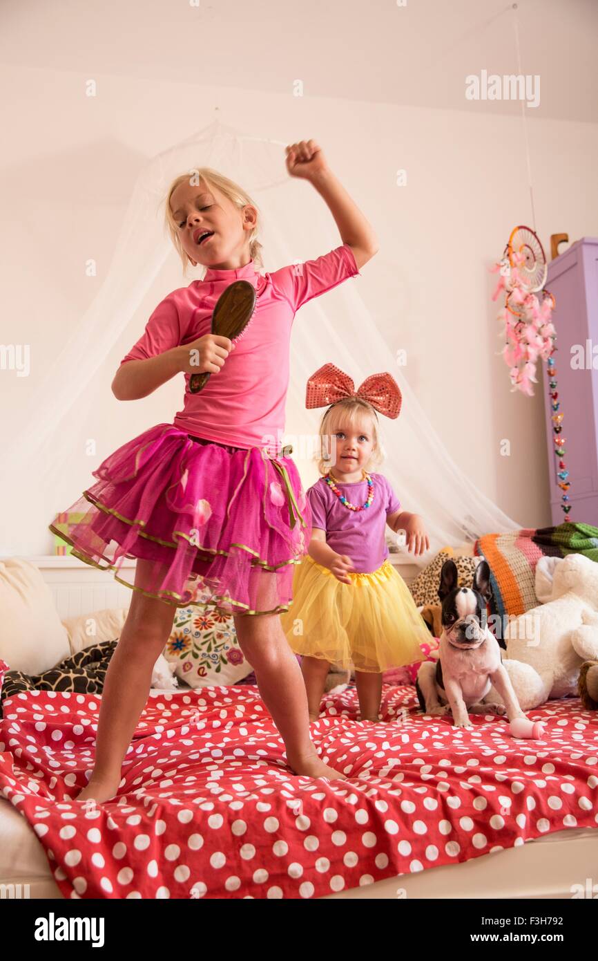 Mädchen und Kleinkind Schwester tanzen und singen mit Mikrofon auf Bett Stockfoto