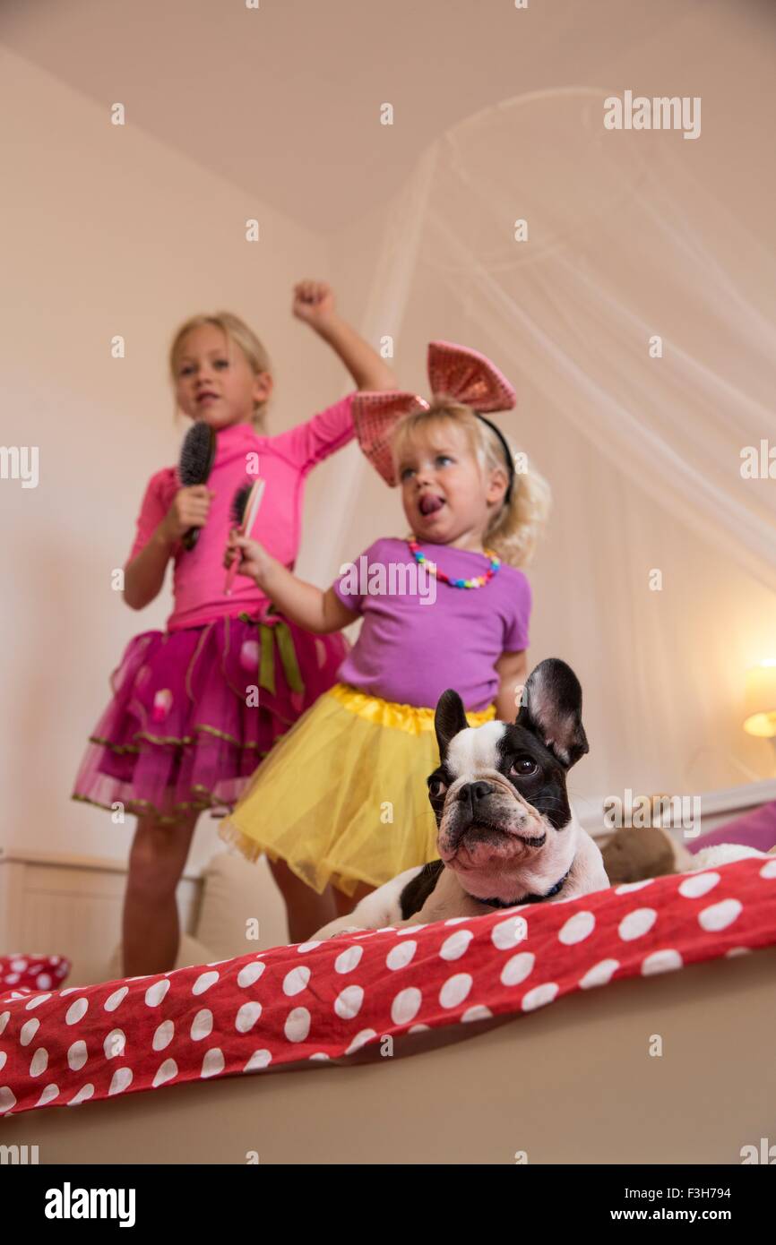 Mädchen und Kleinkind Schwester tanzen und singen mit Mikrofon und Haarbürste auf Bett Stockfoto
