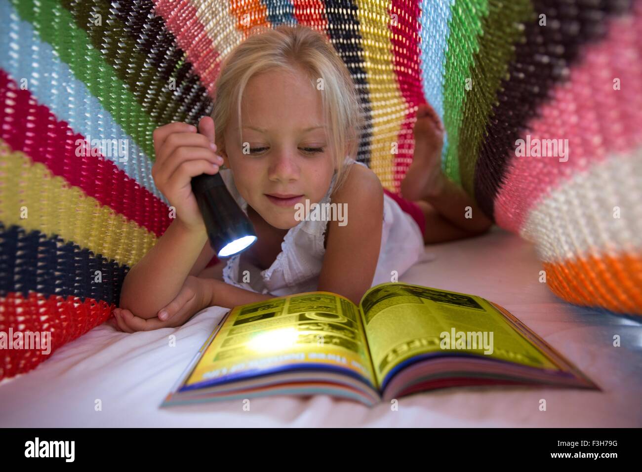 Mädchen auf Bett versteckt unter der Decke und mit Fackel Magazin lesen Stockfoto