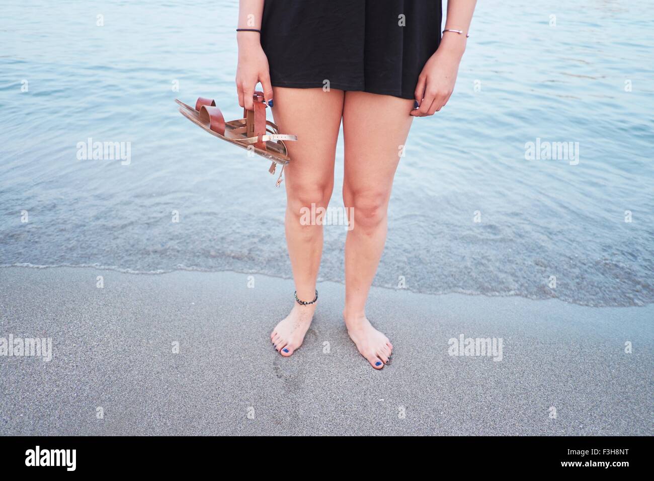 Taille abwärts der jungen Frau am Strand mit Sandalen Stockfoto