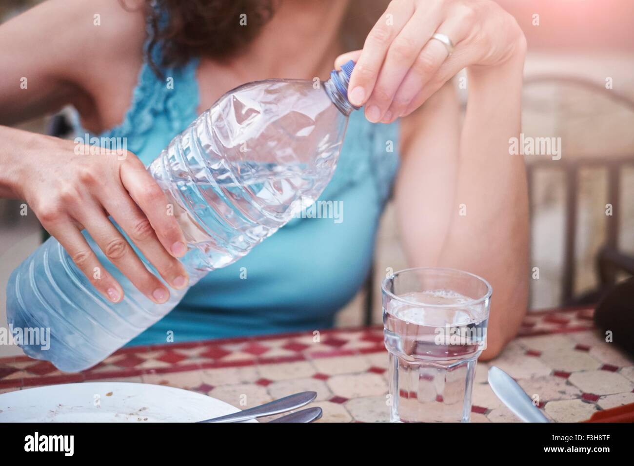 Schuss von Reife Frau Gießen Glas Mineralwasser am Tisch beschnitten Stockfoto