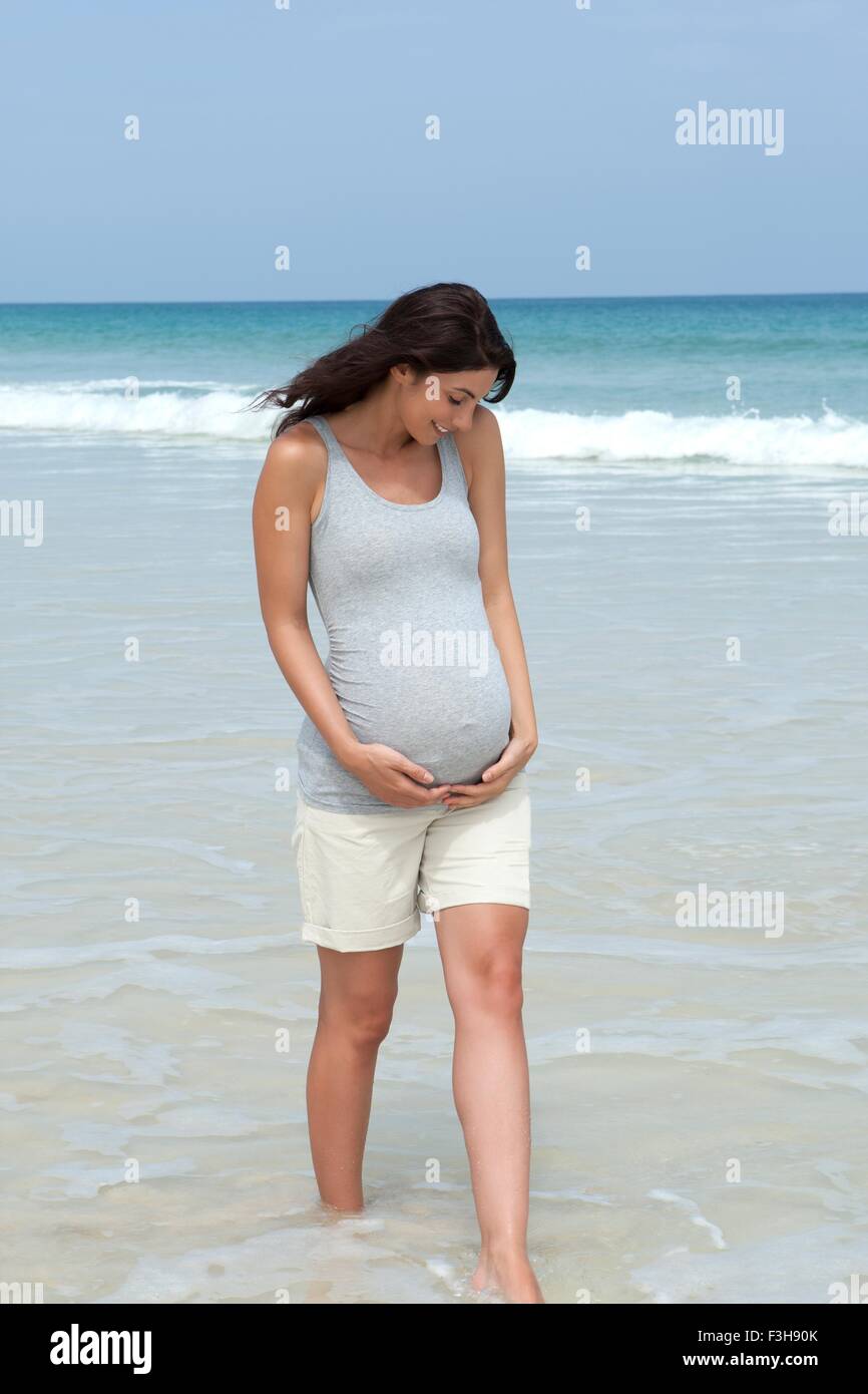 Mitte Erwachsene Frau Paddeln im Meer mit Händen auf Bauch schwanger Stockfoto