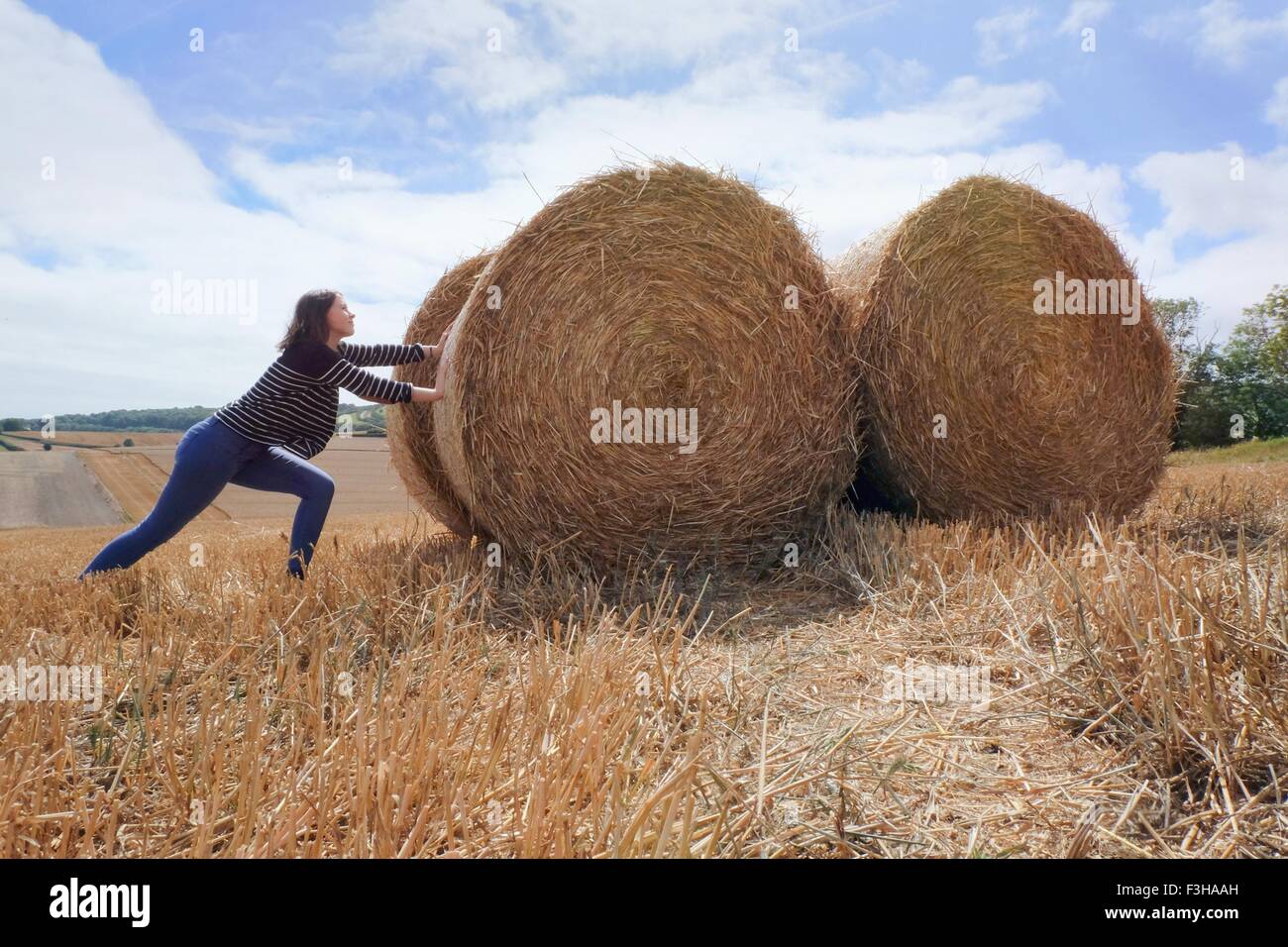 Junge Frau, die vorgibt, Heuhaufen in abgeernteten Feld schieben Stockfoto