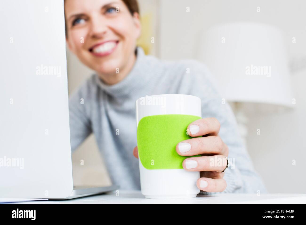 Reife Frau am Laptop halten Tasse lächelnd, Fokus auf Vordergrund Stockfoto