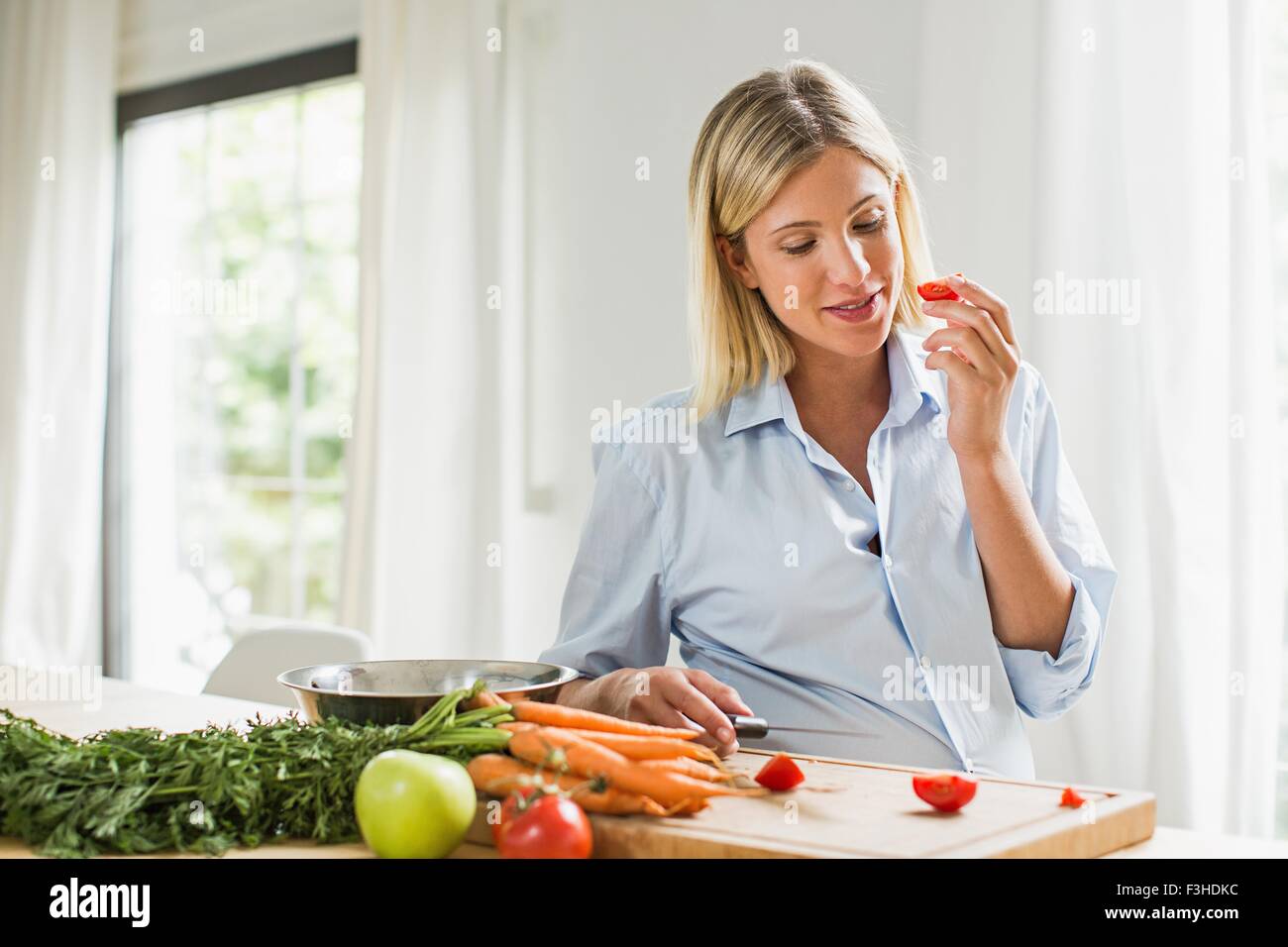 Volle Amtszeit Schwangerschaft junge Frau Essen Tomatenscheibe in Küche Stockfoto