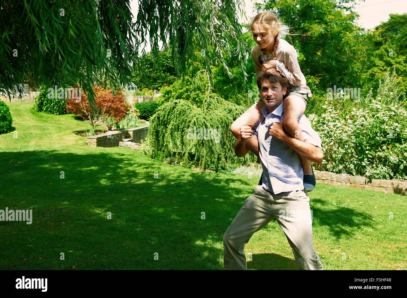 Reifer Mann mit Tochter auf seinen Schultern im Garten Stockfoto