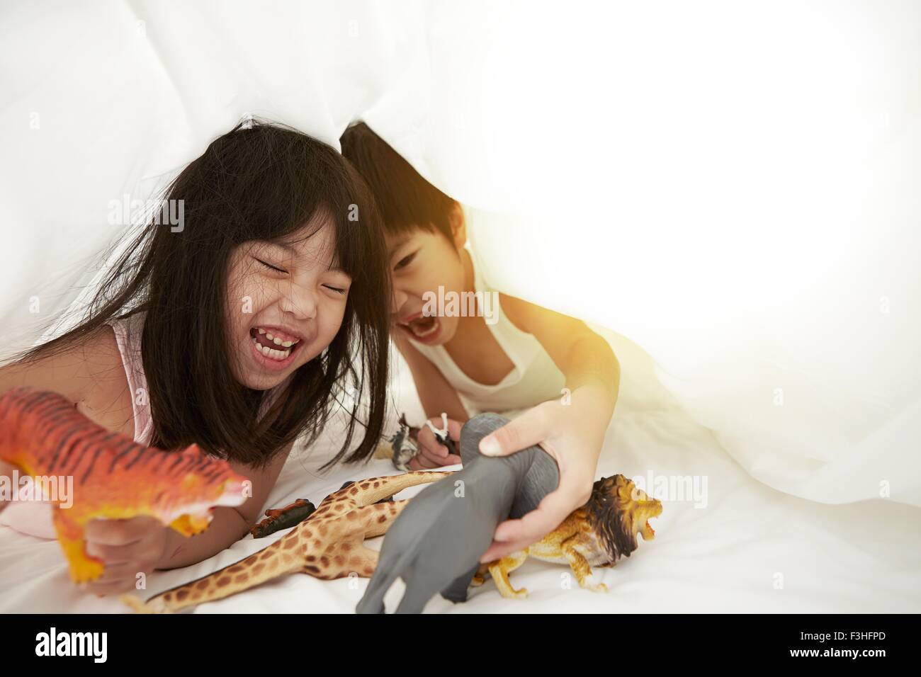 Chinesischen jungen und Mädchen im Bett spielen mit ihren Spielsachen unter der Bettwäsche Stockfoto
