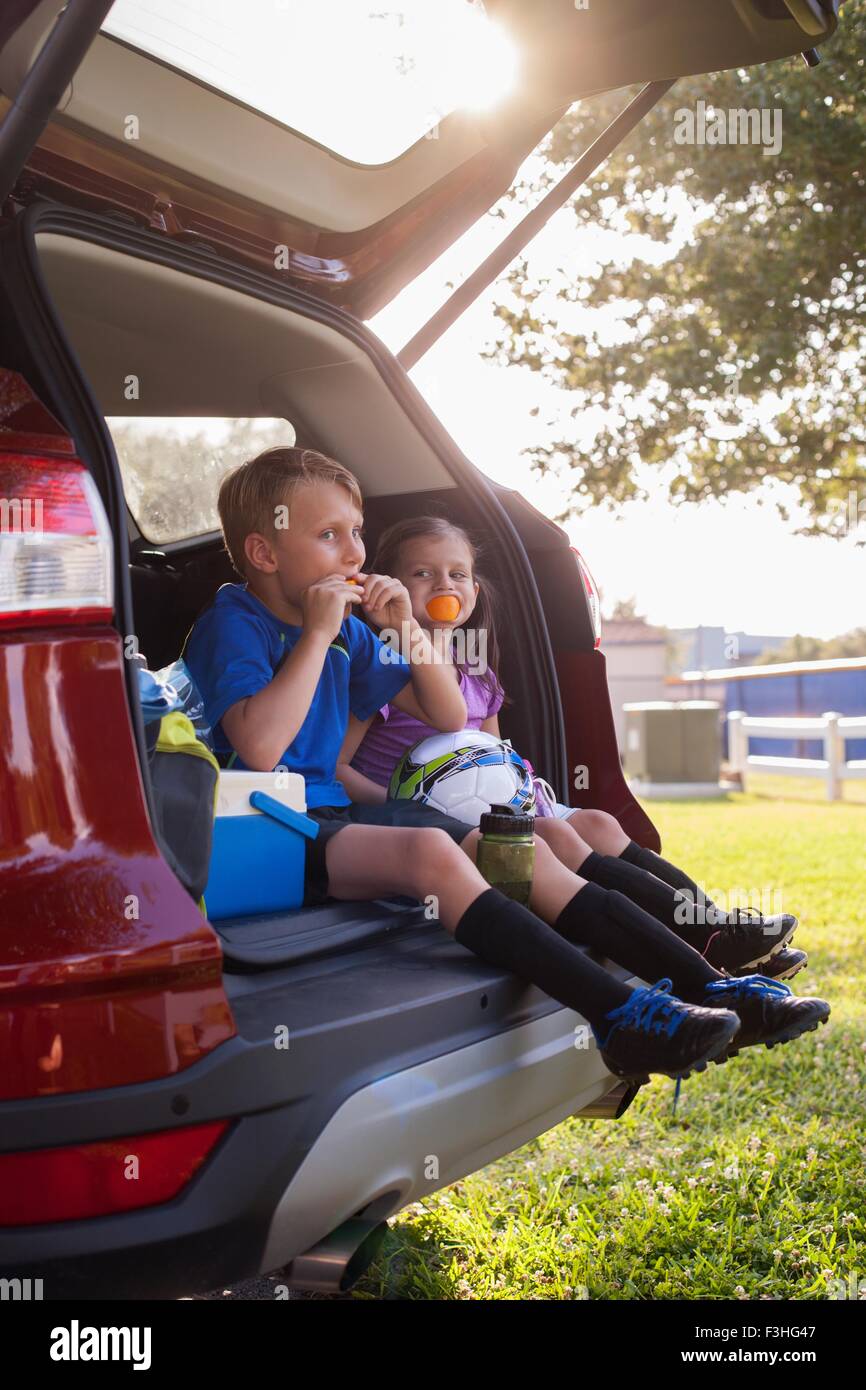 Junge und jüngere Schwester sitzen im Auto boot essende Orangen auf Fußball-Praxis-Pause Stockfoto