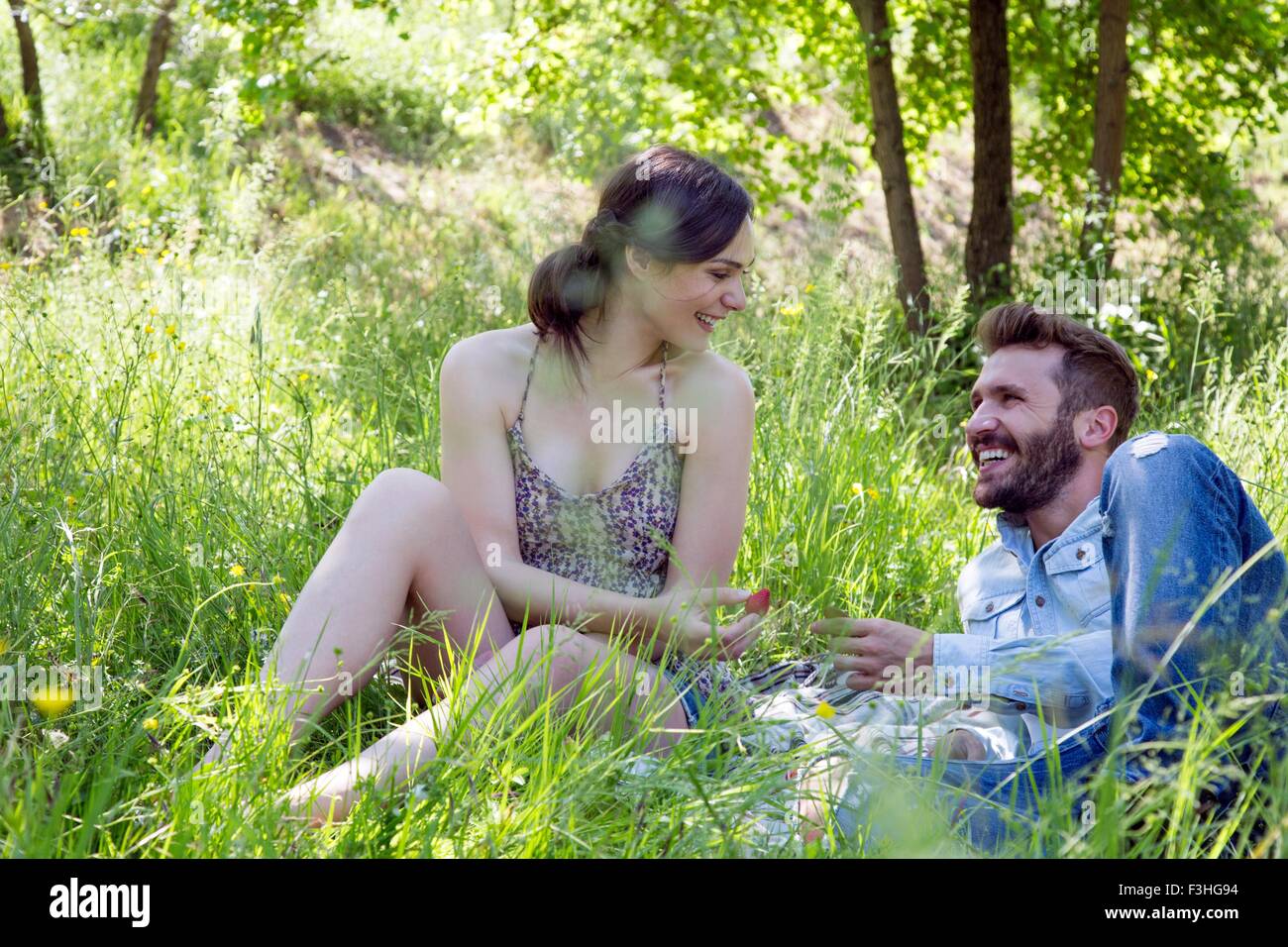 Junges Paar liegen auf dem Rasen von Angesicht zu Angesicht Essen Erdbeeren lächelnd Stockfoto