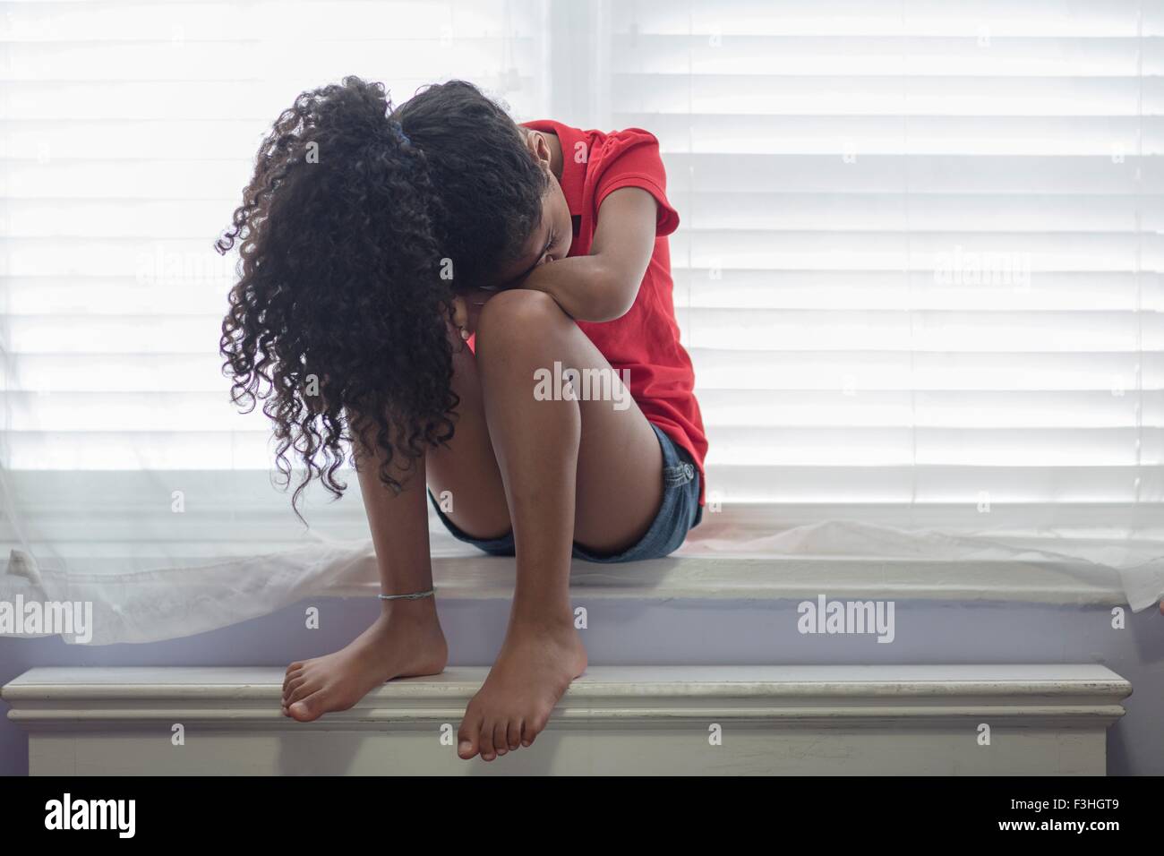 Mädchen sitzen auf der Fensterbank suchen traurig mit Kopf auf Knie Stockfoto