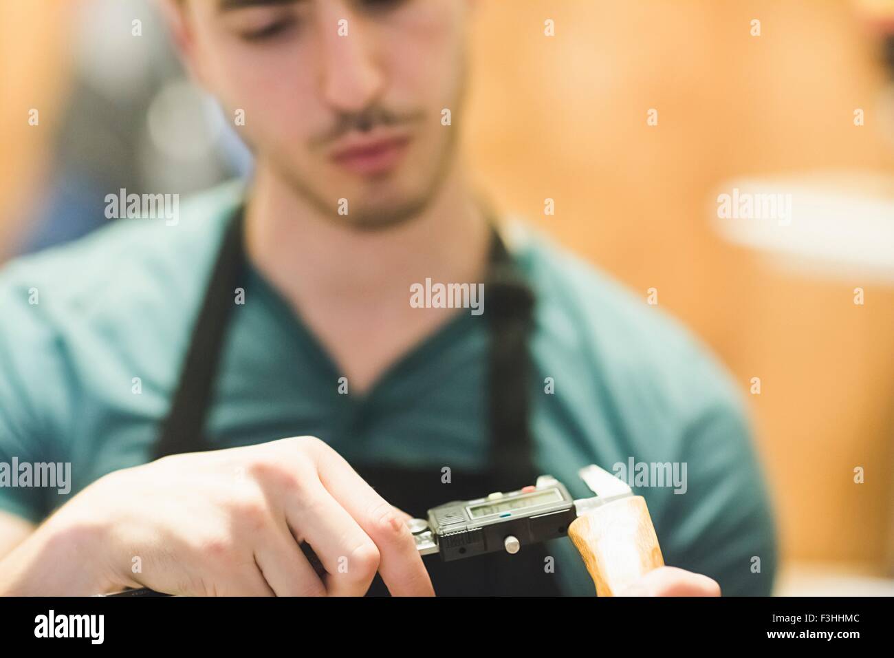 Junger Mann trägt Schürze Handwerk Holz Objekt mit Werkzeug, Blick nach unten Stockfoto
