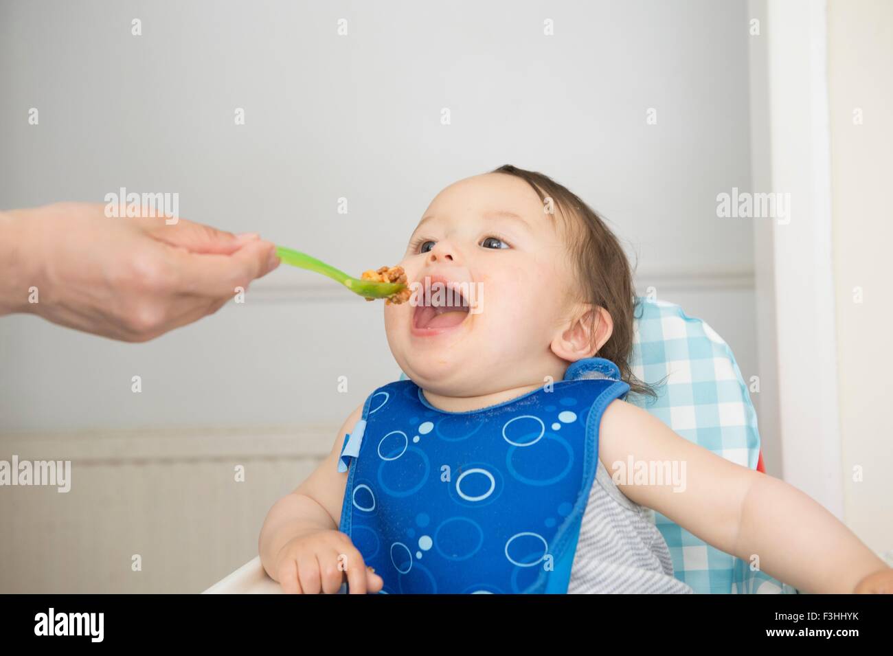 Hand der Mutter Fütterung Babynahrung Küche Hochstuhl Mund Sohn eröffnet Stockfoto
