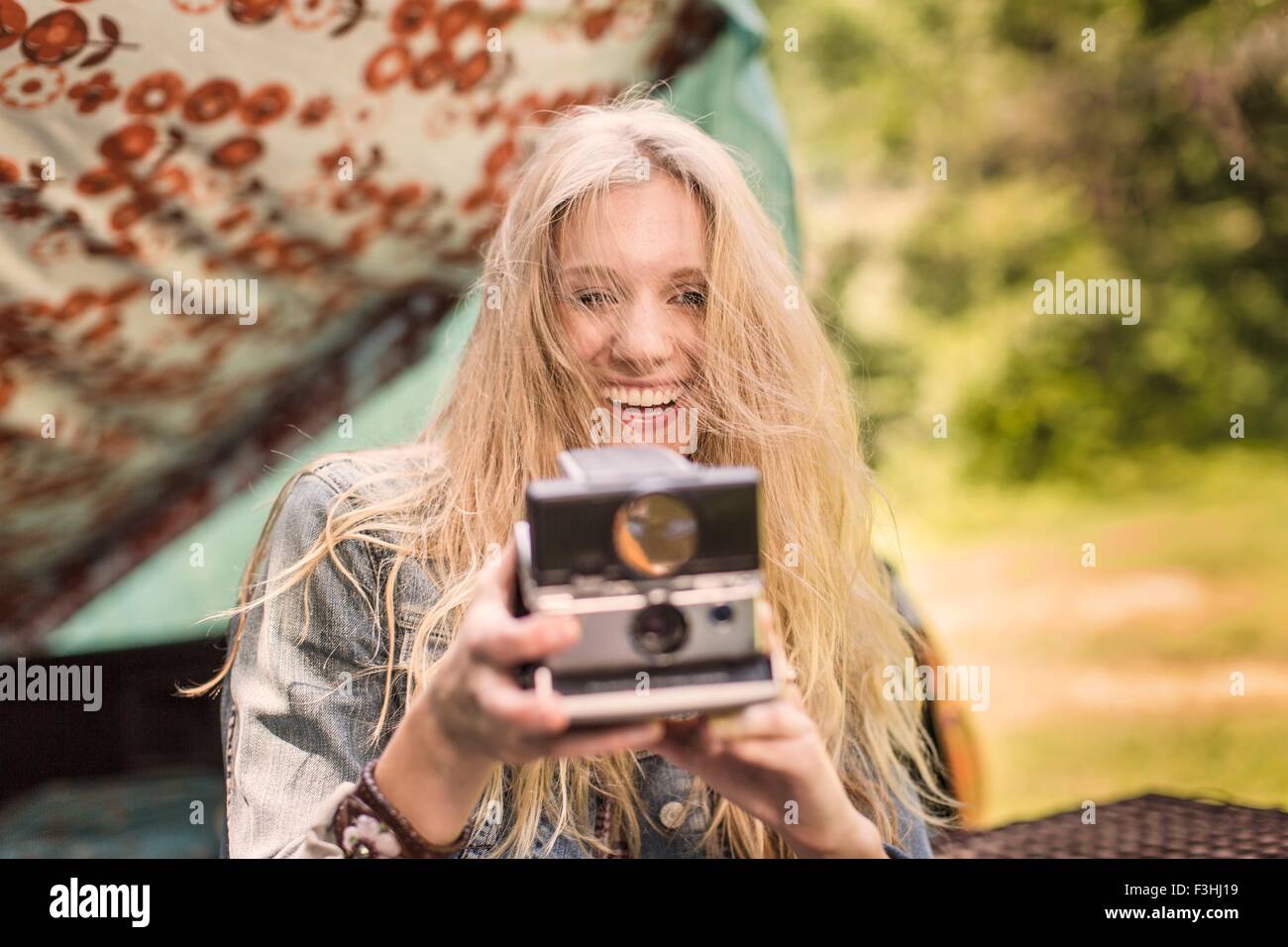 Porträt der jungen Frau mit Sofortbild-Kamera zu fotografieren, während camping Stockfoto