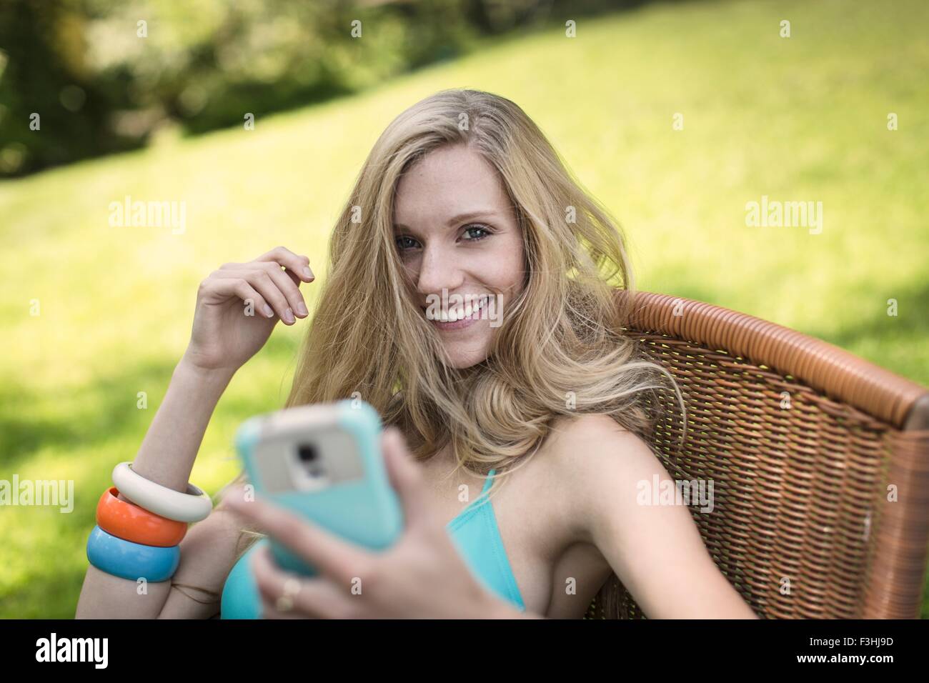 Porträt der jungen Frau mit Bikini-Oberteil mit Smartphone im Garten Stockfoto