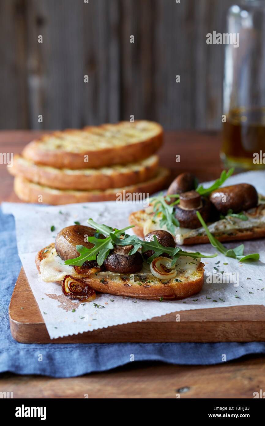 Stillleben mit Bruschetta mit Portobello Pilze gebraten Cipollini Zwiebel, Gouda-Käse und frischem Rucola Stockfoto