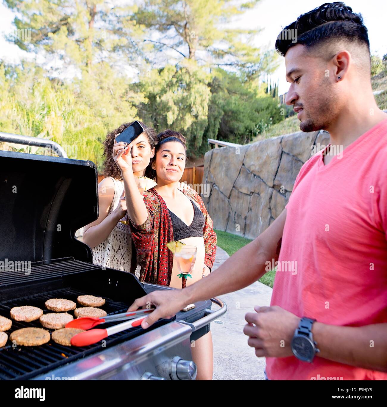 Junger Mann am Grill vor Schwestern unter Smartphone Selfie Kochen Stockfoto