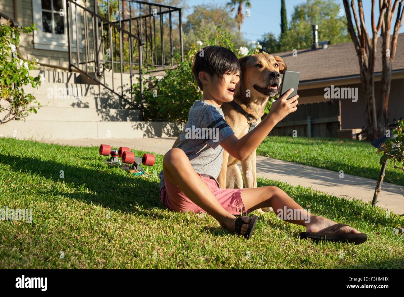 Junge posiert für Smartphone Selfie mit Hund im Garten Stockfoto