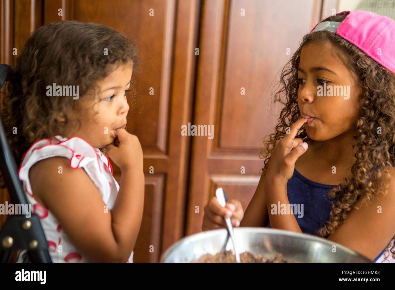 Schwestern von Angesicht zu Angesicht Finger im Mund Verkostung Schokoladenkuchen mischen Stockfoto