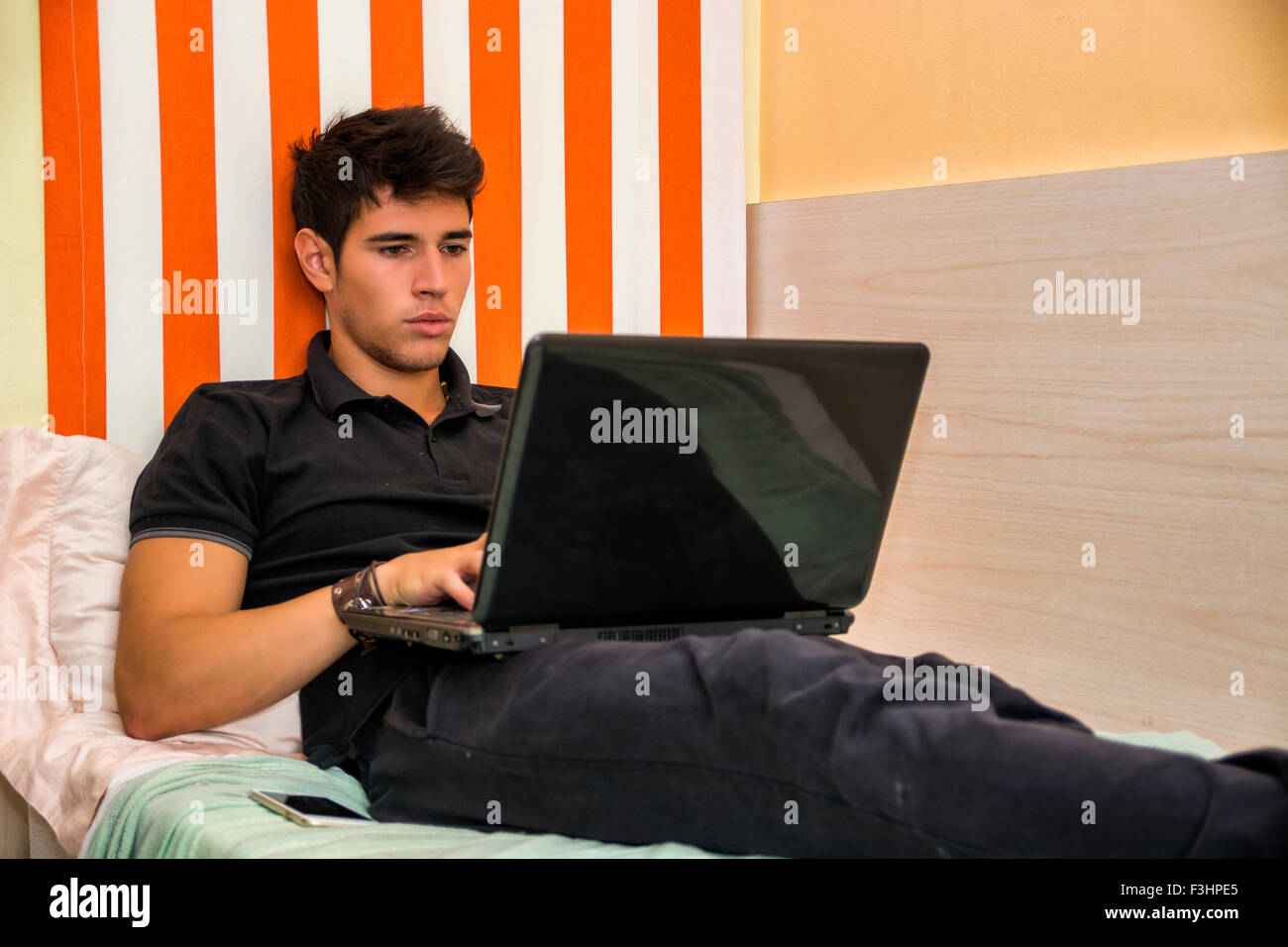 Attraktiver junger Mann mit schweren Ausdruck, bequem liegend, mit Laptop am Bett arbeiten auf seine Start-up - Young Stockfoto