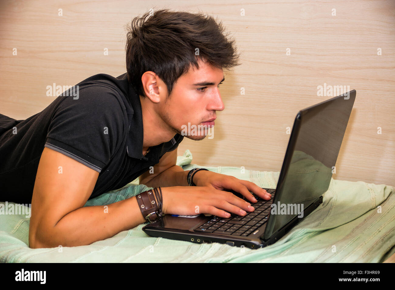 Attraktiver junger Mann mit schweren Ausdruck mit Laptop am Bett arbeiten an seiner Firmengründung - Young Male College oder Universität Stockfoto