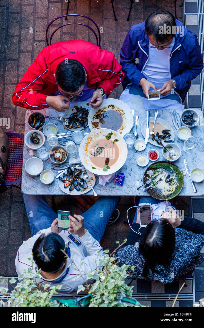 Touristen, die Fisch und Meeresfrüchte essen, während mit Smartphones, königliche Gericht, Carnaby Street, London, UK Stockfoto