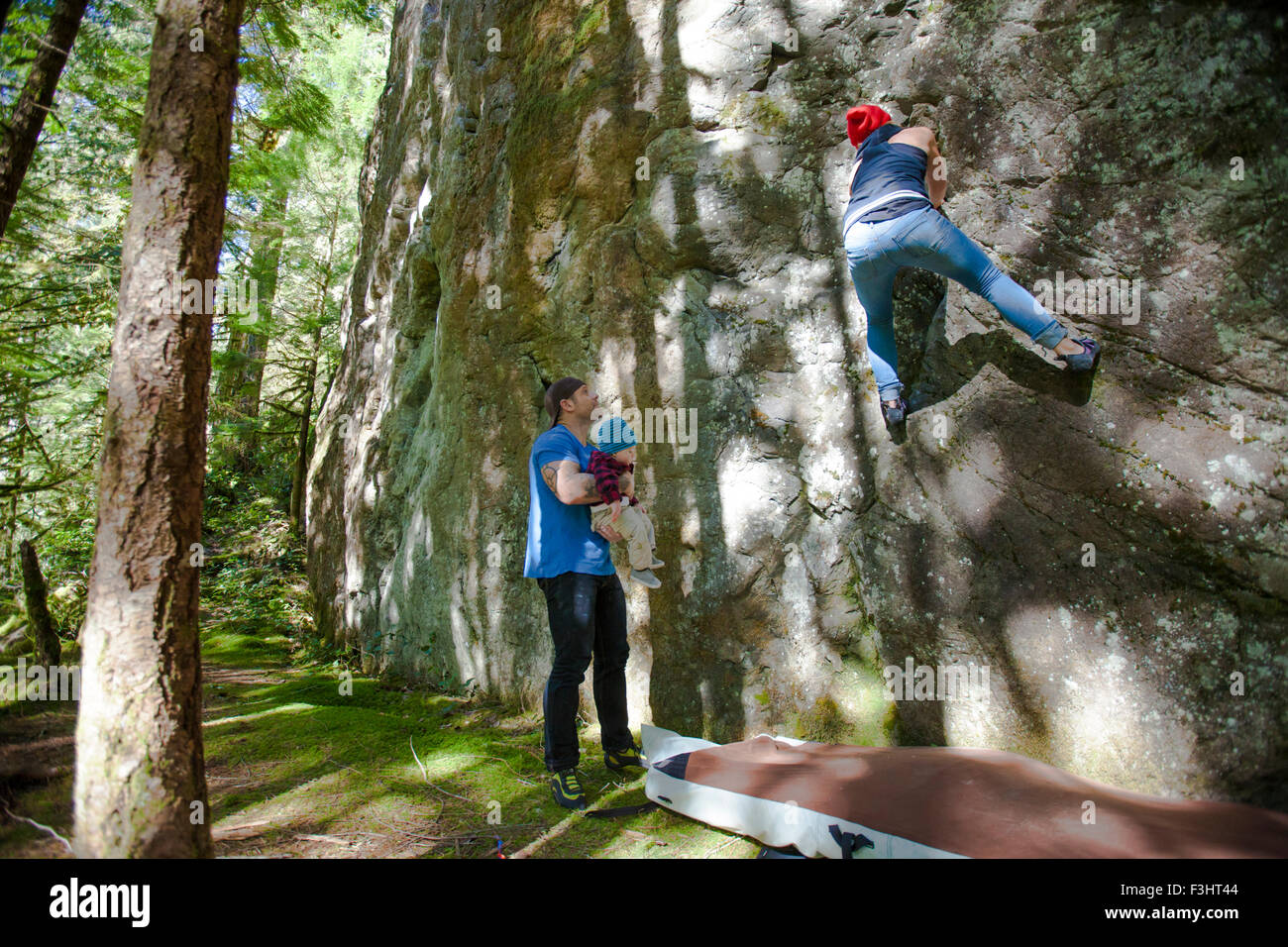 Ein Vater hält seinen Sohn während seiner Frau Felsbrocken auf einer Felswand. Stockfoto