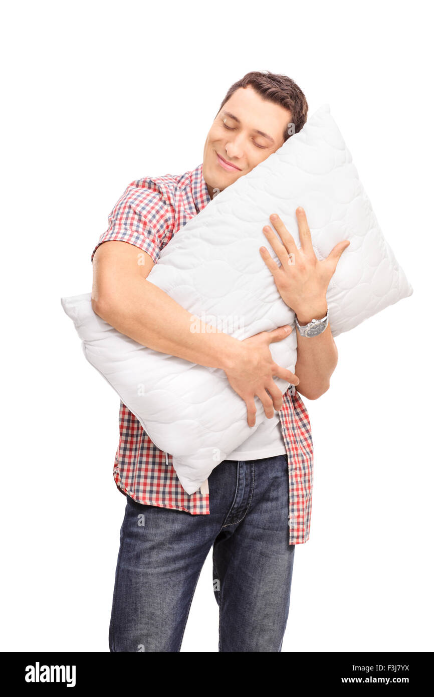 Vertikale Schuss von einem fröhlichen jungen Mann umarmt eine Kissen mit seinen Augen geschlossen isolierten auf weißen Hintergrund Stockfoto