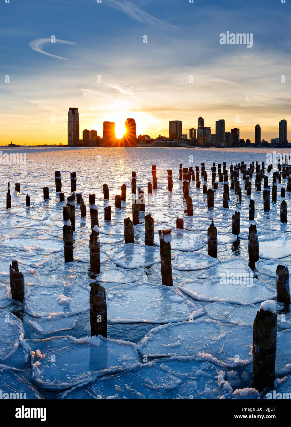 Holz Pfähle aus New York alten Pier bei Sonnenuntergang mit Jersey City Gebäude durch das Eis am Hudson Fluss herausragen Stockfoto