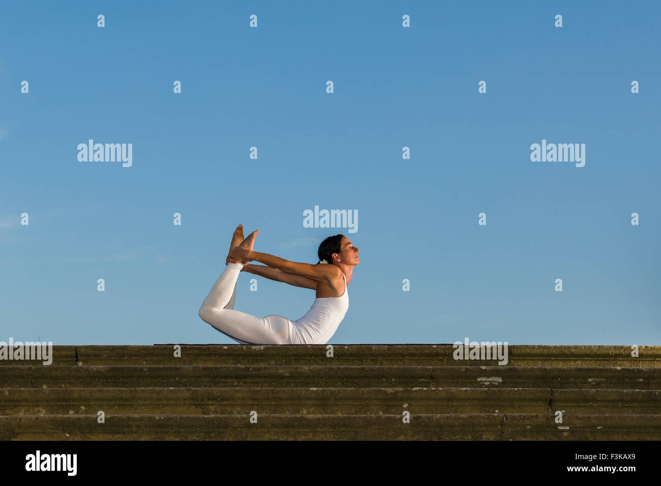 Junge Frau, eine weiße Babybody, übt Hatha-yoga Outdoor, zeigt die Pose: dhanurasana, Bogen Stockfoto