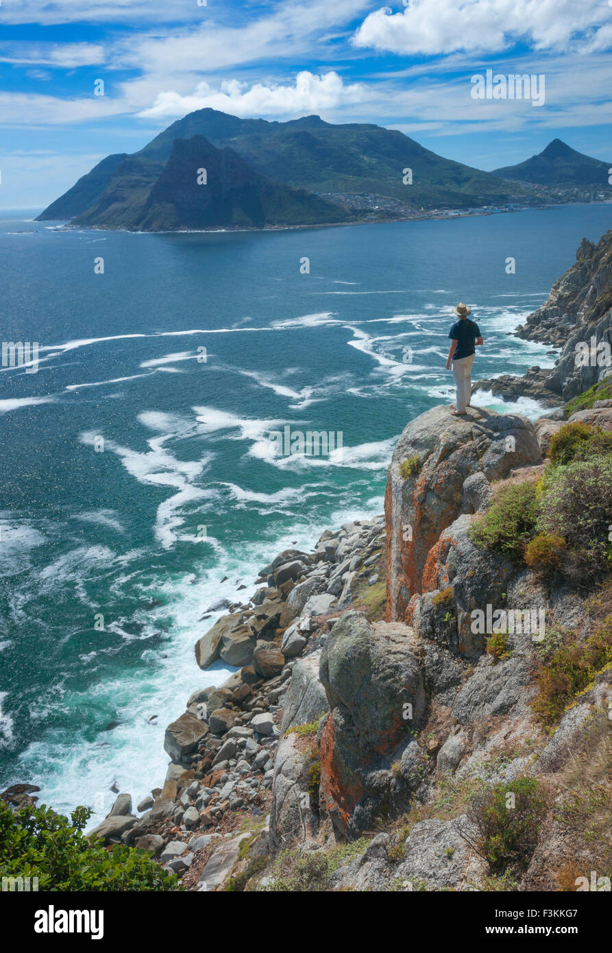 Ein einsamer Wanderer auf Felsen über dem Atlantischen Ozean blickt in Richtung Sentinel Peak, Seelandschaft von Chapmans Peak Drive betrachtet Stockfoto