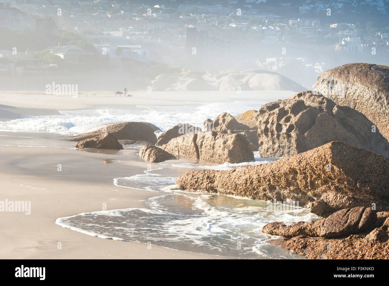 Des Camps Bay Beach in der Morgendämmerung mit Person zu Fuß Hund im Nebel entlang der Ufer des Atlantischen Ozean, Cape Town, Südafrika Stockfoto