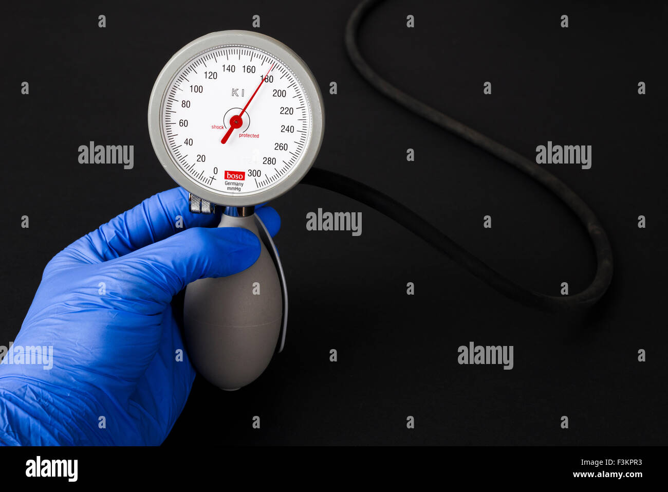 Eine Hand in einem blauen medizinische Handschuh hält ein sphygomanometer, Blutdruckmessgerät, für medizinische Zwecke, die Angabe hoher Blutdruck pressu Stockfoto