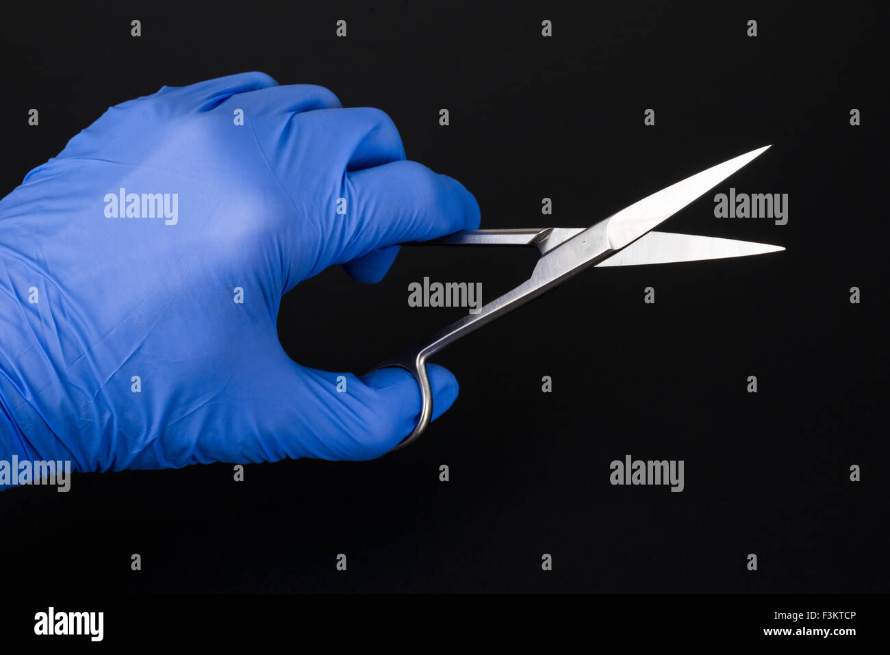 Eine Hand in einem blauen medizinische Handschuh hält eine Schere für medizinische Zwecke, die auf einem schwarzen Tabelle angezeigt Stockfoto