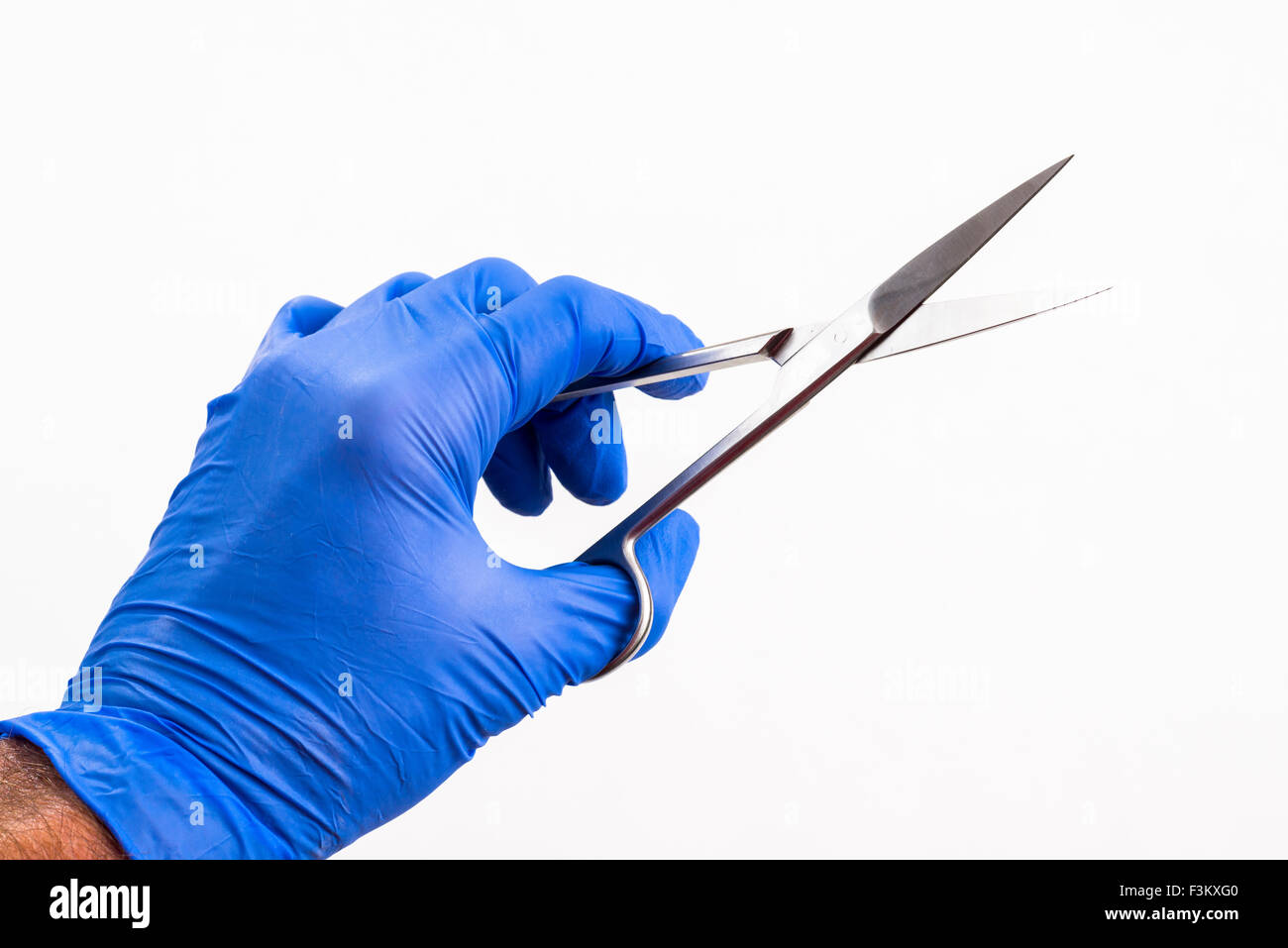 Eine Hand in einem blauen medizinische Handschuh hält eine Schere für medizinische Zwecke, die auf einem weißen Tabelle angezeigt Stockfoto