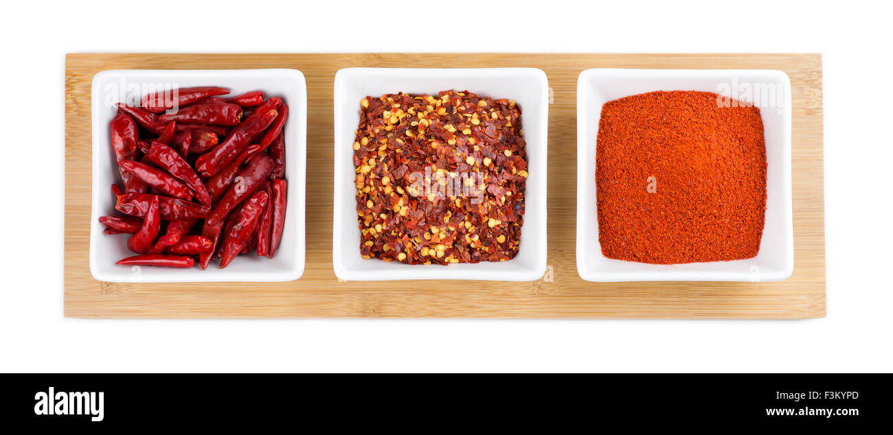 Isolierte Chilischoten in verschiedenen Formen aus frischen Flocken und Pulver in weißen Schalen auf einer hölzernen Plattform Stockfoto
