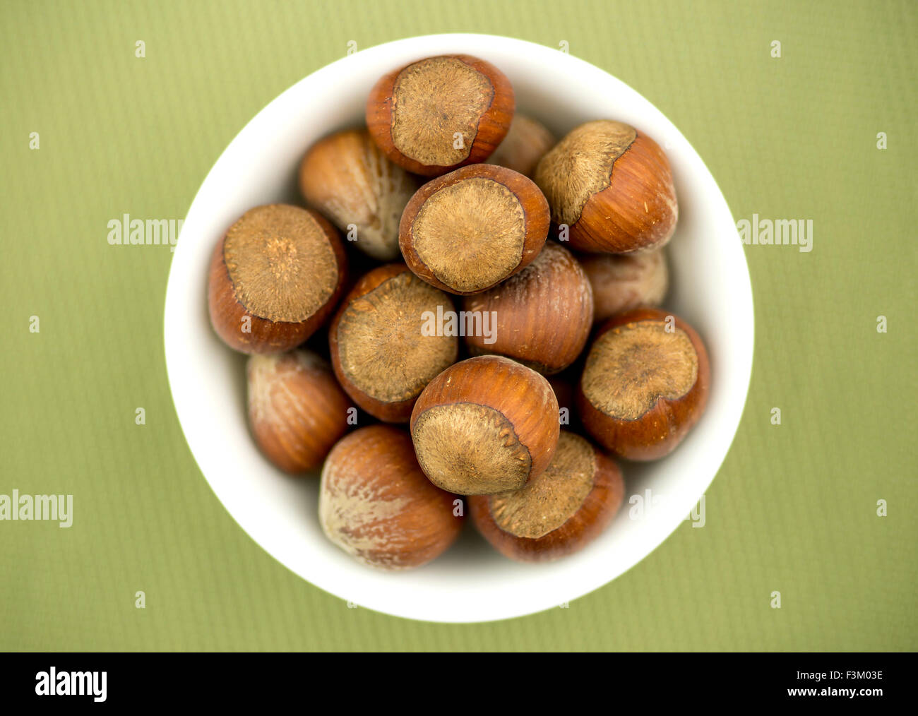 Schüssel mit Haselnüssen gegen strukturierten grünen Hintergrund Stockfoto