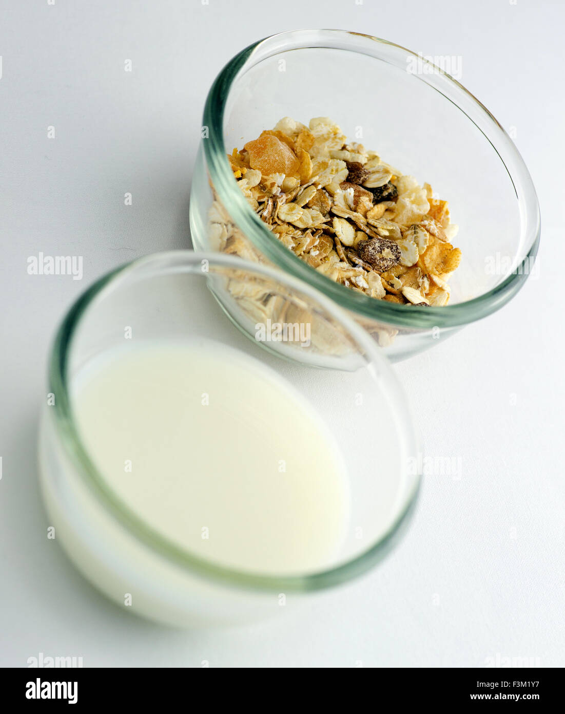 Fettarme Milch mit Müsli und Müsli in transparenten Schalen vor einem weißen Hintergrund Stockfoto