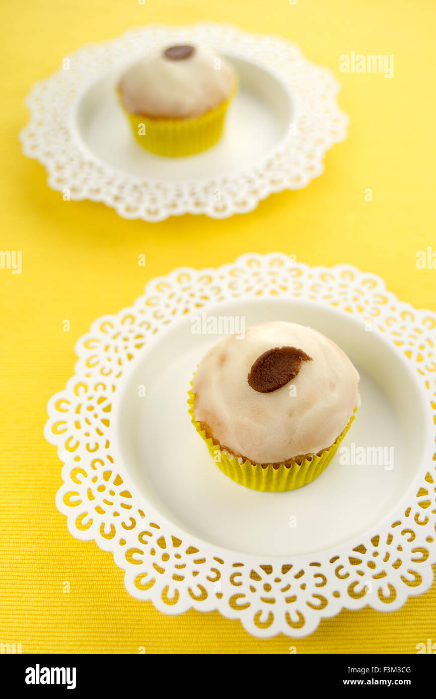 Glasierten Vanille Cupcakes auf ausgefallenen Platten gegen einen gelben strukturierten Hintergrund serviert. Geringe Schärfentiefe mit Fokus auf Vorderseite. Stockfoto