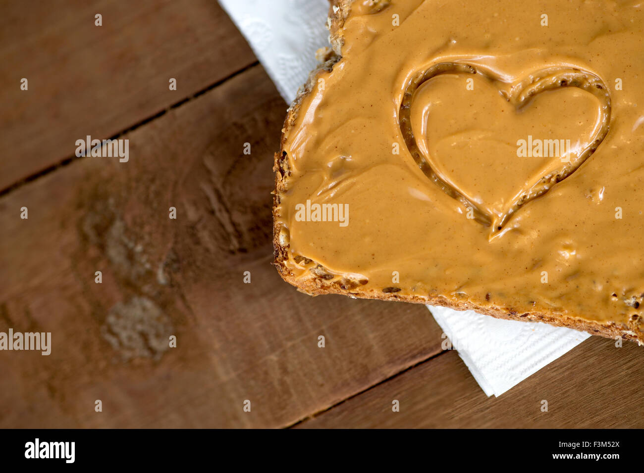 Nahaufnahme von Erdnussbutter Toast mit Herzform auf Gewebe gegen Holz Stockfoto